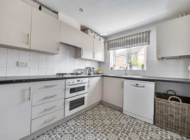 Kitchen with white cabinets, integrated oven, worktops and a window.