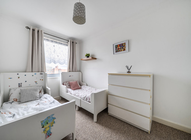 Children's bedroom with two single beds, dresser, and wall pictures.
