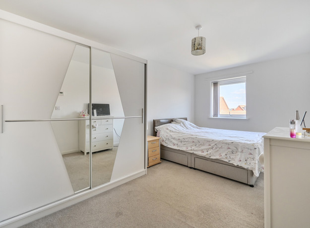 Bedroom with mirrored wardrobe, bed, and chest of drawers.