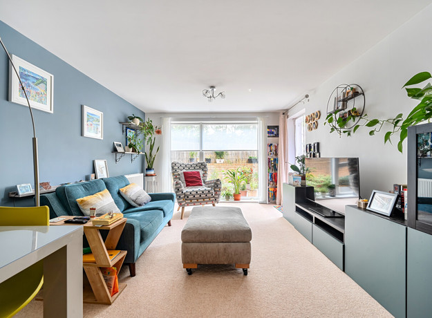 Living room with sofa, footstool, shelving unit and large window.