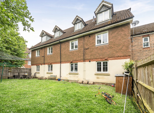 Rear view of terraced houses with lawn garden and fenced boundary.
