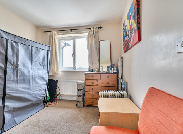 Single bedroom in a modern home with window, carpeted flooring, chest of drawers and built-in storage space.