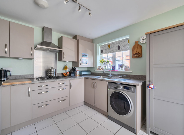 Kitchen with fitted cabinets, washing machine and tiled floor.