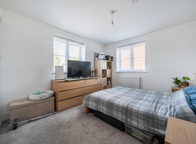 Bedroom with double bed, chest of drawers, TV and windows.