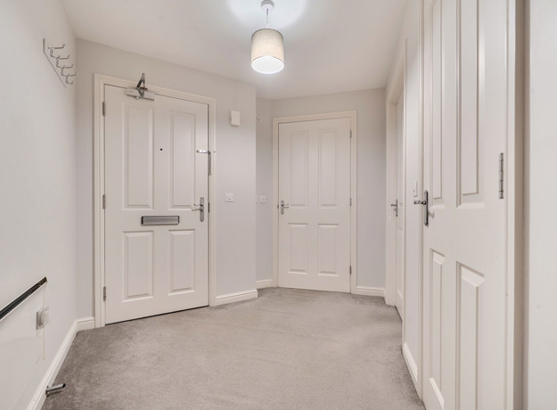 Hallway with multiple doors, radiator and carpeted flooring.