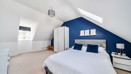 Bedroom with sloped ceiling, blue accent wall, neatly made double bed and white wardrobe.
