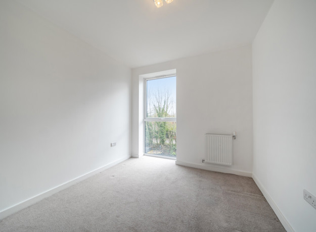 Carpeted bedroom with white walls, radiator, and large window