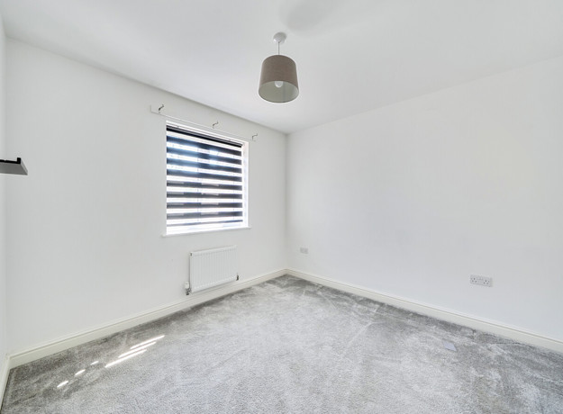 Empty bedroom with grey carpet and window with blind.