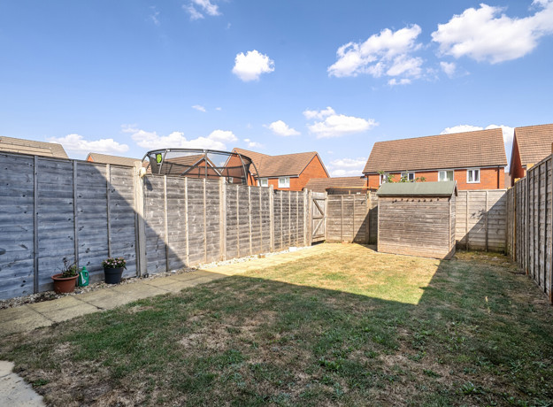 Enclosed rear garden with lawn, paved path, shed and wooden fencing.