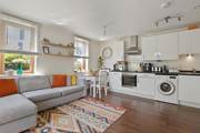 Open plan room with sofa, kitchen units, table, and window with blinds.