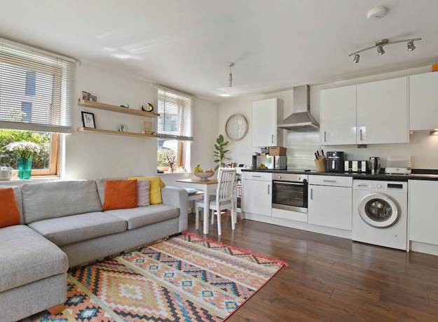 Open plan room with sofa, kitchen units, table, and window with blinds.