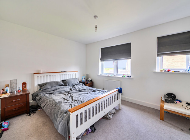 Bedroom with double bed, bedside tables, and two windows with blinds.