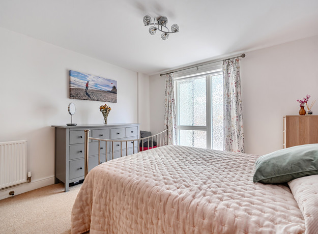 Bedroom with double bed, chest of drawers and window with curtains.