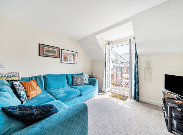 Living room with blue corner sofa and doors leading to a balcony.