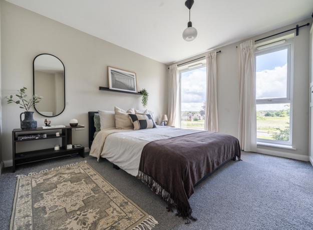 Bedroom with bed, bedside table, mirror, rug, and large windows with curtains.