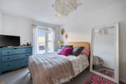 Bedroom with double bed, cushions, dresser, and mirror against a light wall.