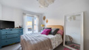 Bedroom with double bed, cushions, dresser, and mirror against a light wall.