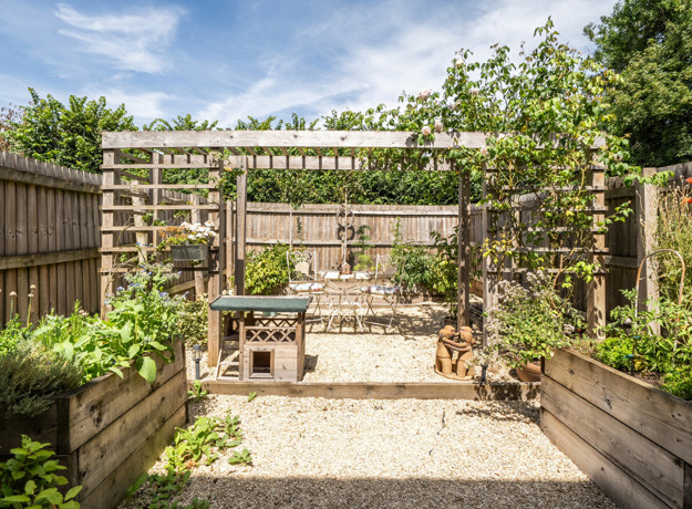 Garden with pergola, gravel area, raised beds, and fencing.