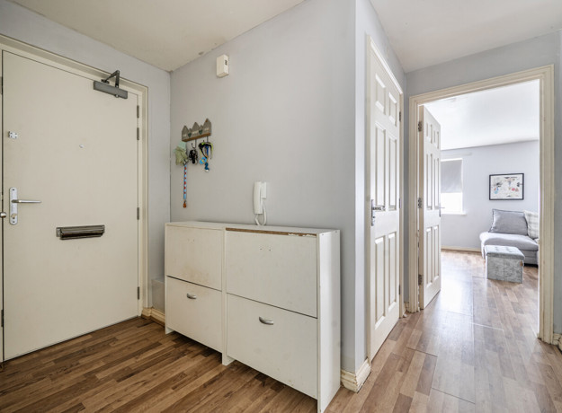 Hallway with wooden-effect floor, radiator, cabinet and view into another room.