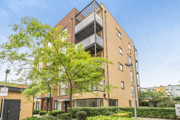 Apartment building with balconies and trees along a landscaped footpath.