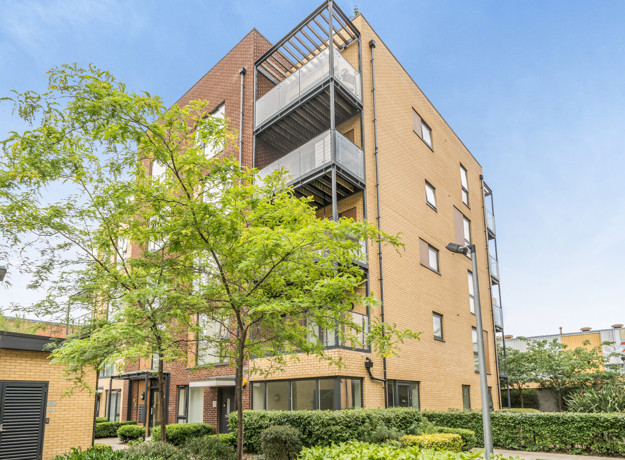 Apartment building with balconies and trees along a landscaped footpath.