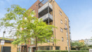 Apartment building with balconies and trees along a landscaped footpath.