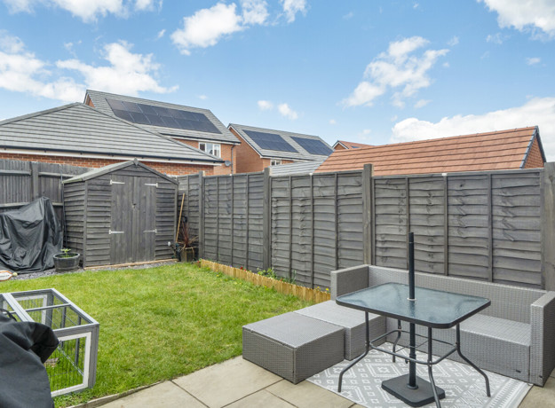 Garden with patio seating, lawn, and wooden fencing under blue sky.