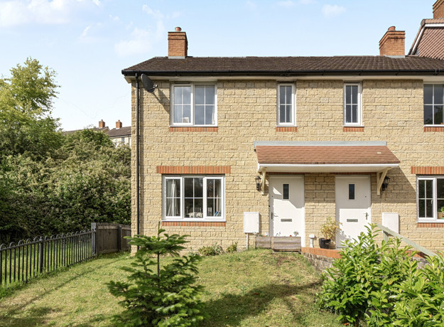 Two storey end-of-terrace brick house with front garden, path and white door.