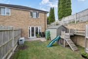 Rear view of the house with a fenced garden with paved patio and play equipment.