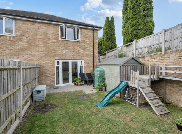 Rear view of the house with a fenced garden with paved patio and play equipment.