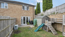 Rear view of the house with a fenced garden with paved patio and play equipment.