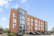 Modern apartment building with red brick and grey cladding, with cars parked in front