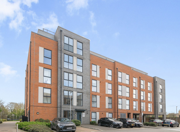 Modern apartment building with red brick and grey cladding, with cars parked in front
