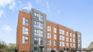 Modern apartment building with red brick and grey cladding, with cars parked in front