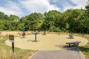 Outdoor exercise area with fitness equipment beside a tree-lined green space.