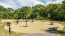 Outdoor exercise area with fitness equipment beside a tree-lined green space.