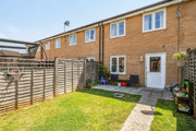 Rear garden with a lawn, fenced boundaries and the back of a brick house.