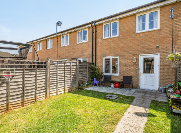 Rear garden with a lawn, fenced boundaries and the back of a brick house.