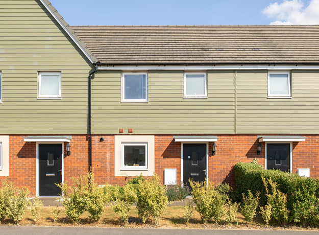 Row of terraced houses with front gardens and paved walkway.