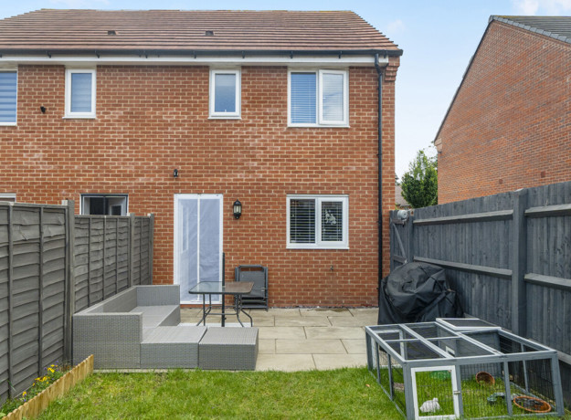 Rear view of brick house with patio, lawn, and fenced garden.