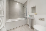 Bathroom with bathtub, shower screen, sink, toilet, and tiled walls.