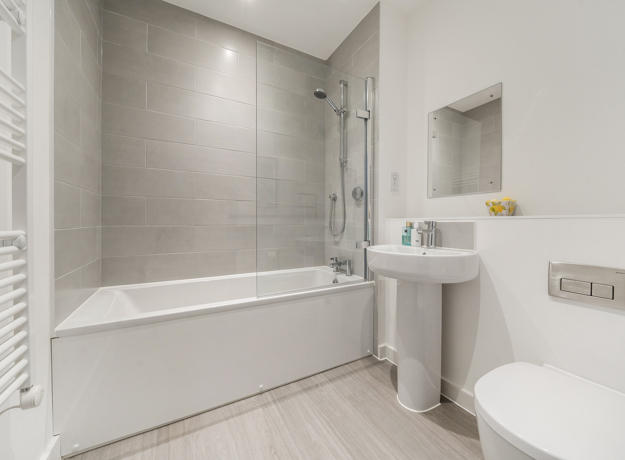 Bathroom with bathtub, shower screen, sink, toilet, and tiled walls.