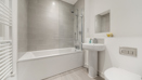 Bathroom with bathtub, shower screen, sink, toilet, and tiled walls.