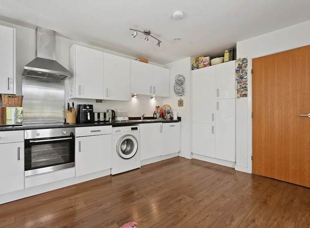 White kitchen with oven, washing machine, cabinets, and wooden floor.