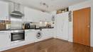 White kitchen with oven, washing machine, cabinets, and wooden floor.