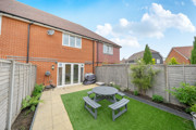 Back garden with patio, lawn, table and chairs enclosed by fencing.