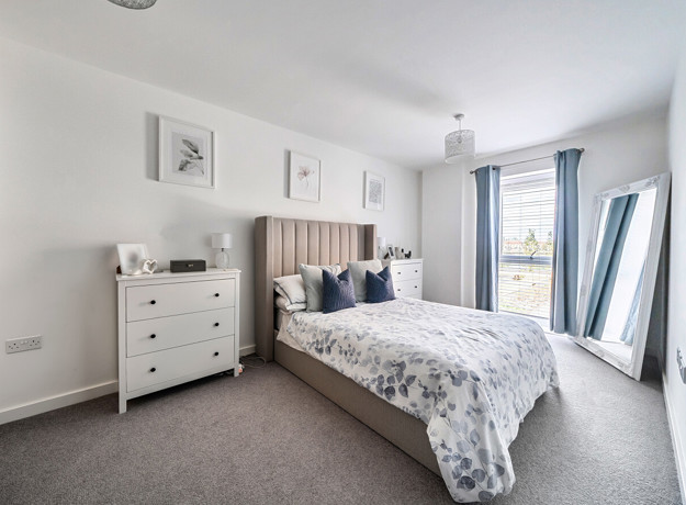 Bedroom with double bed, chest of drawers and windows with curtains.