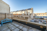 Paved balcony with metal railing overlooking nearby houses and blue sky.