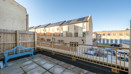 Paved balcony with metal railing overlooking nearby houses and blue sky.