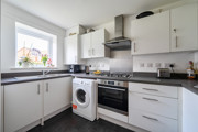 Modern fitted kitchen with white units, sink, oven, washing machine and window over the worktop